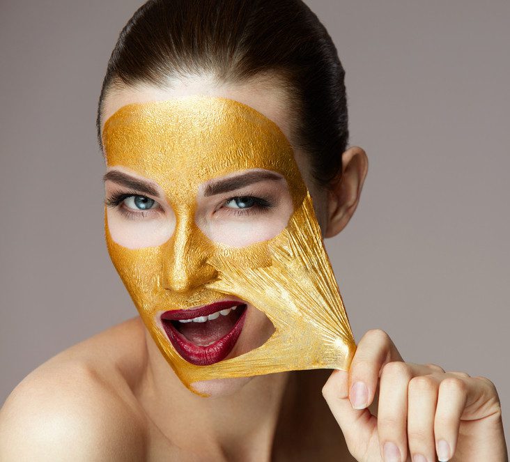 Image of woman pulling at gold mask on face