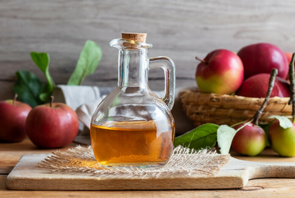 bottle of apple cidar vinegar surrounded by apples